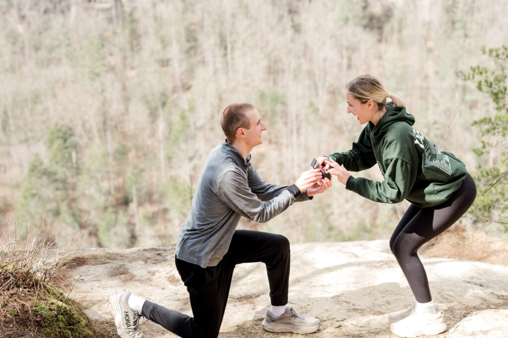 Jake kneeling on one knee at Sky Bridge in Red River Gorge, proposing to a surprised Mallory