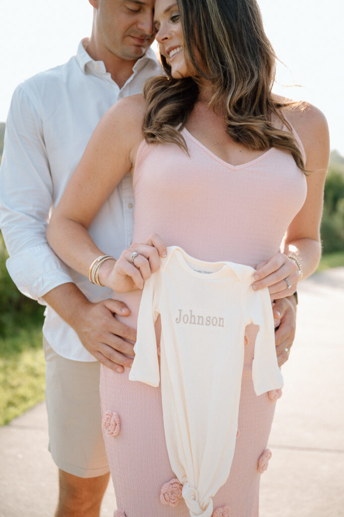 Pregnancy reveal in Louisville KY with parents holding baby girl outfit